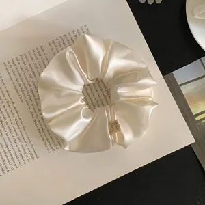 Elegant creamy white satin scrunchie hair tie detail view on an open book prop