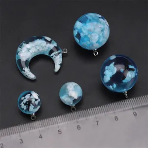 Close-up detail of blue sky and cloud resin pendants with a ruler for size reference