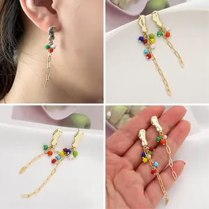 Close-up of golden irregular stud earrings with vibrant colorful beads and long chain drops