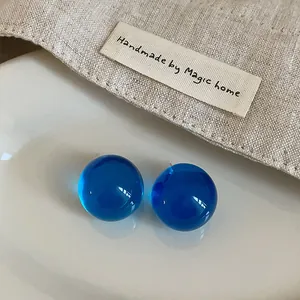Close-up detail of vibrant blue transparent resin stud earrings on a textured linen background