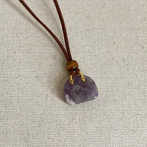 Detailopname van een paarse natuurstenen handtas hanger aan een bruin suède koord