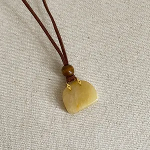 Detailopname van een handtasvormige gele natuurstenen hanger aan een bruine koordketting