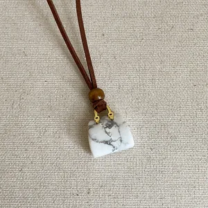 Detail van een wit marmeren handtas hanger aan een bruine koord ketting voor dames