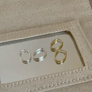 Dettaglio di orecchini a cerchio ovali minimalisti in oro e argento su base a specchio