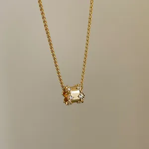 Close-up van een gouden ketting met cilindervormige hanger en sprankelende kristallen