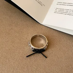 Primo piano di un anello aperto color argento con un fiocco di corda nera e rilievi planetari.