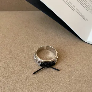 Primo piano di un anello aperto d'argento con motivo a pianeti e un fiocco di corda nera
