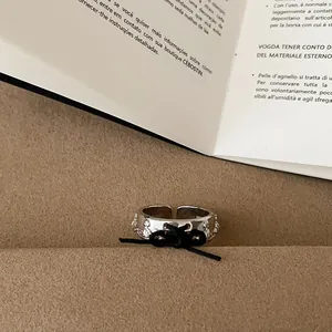 Primo piano dell'anello aperto in argento con fiocco in corda nera e motivi planetari.