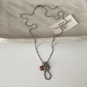 Detailopname van een zilveren kralenketting met een getextureerde schijf en rode paddenstoel.