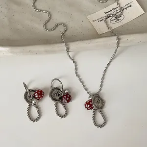 Detail van zilveren ketting en oorbellen met rode paddenstoelhangers en parelaccenten