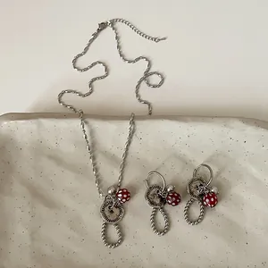 Gedetailleerd overzicht van zilveren knoop en rode stip paddenstoel ketting en oorbellen