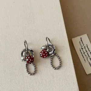 Detailweergave van niche-oorbellen met rode stippen kralen en parel accenten