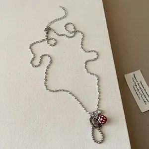 Detailweergave van een zilveren kralenketting met knoophanger en een rode bedel.
