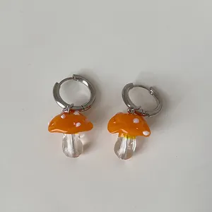 Makro-Detail von handgefertigten orangefarbenen Pilz-Ohrringen aus Glas auf Weiß.