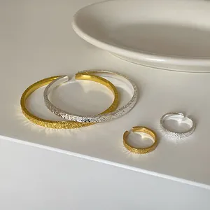 Nahaufnahme von strukturierten, gehämmerten offenen Armbändern und Ringen in Gold und Silber.