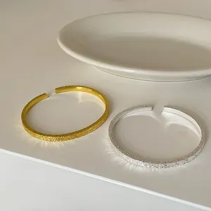 Detailansicht von eleganten gehümmerten offenen Armreifen in Gold- und Silberoptik.