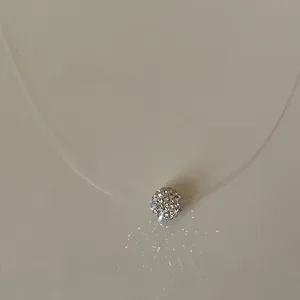 Close-up detail of a minimalist transparent fish line necklace with crystal ball pendant.