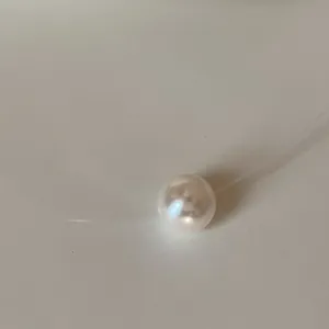Close-up detail of a minimalist white pearl pendant on a clear fishing line necklace