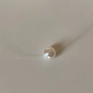 Close-up detail of a minimalist white pearl pendant on an invisible fishing line cord.
