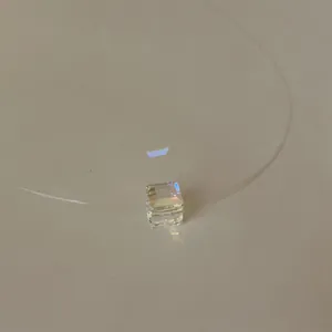 Macro view of an iridescent cube pendant on a transparent fishing line necklace cord.