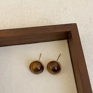 Detail shot of round brown resin stud earrings with gold bezel in a wooden tray.