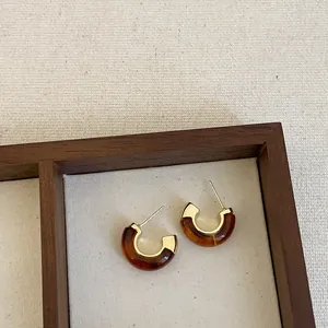 Close-up of C-shaped brown resin earrings with gold accents displayed in a wooden tray