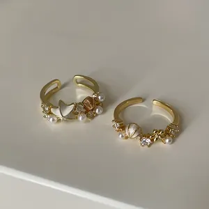 Detailansicht von goldenen verstellbaren Ringen mit Zirkonia, Perlen, Muscheln und Blumen.