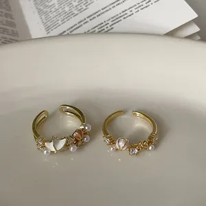 Detaillierte Makroansicht eleganter vergoldeter offener Ringe mit Zirkon- und Perlschalenakzenten