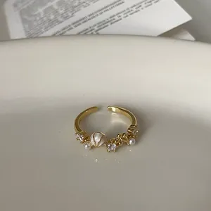 Nahaufnahme eines eleganten goldenen Rings mit Zirkon-, Perlen- und Muschelmotiven