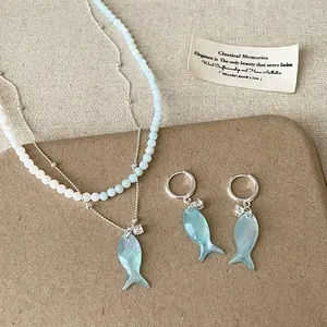 Dettaglio di collana con ciondolo a pesce in conchiglia blu e orecchini a cerchio