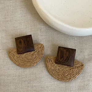Macro view of geometric wood and woven straw earrings showing detailed craftsmanship