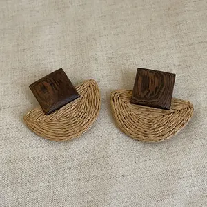 Detailed view of geometric earrings with dark wood square and woven straw accents.