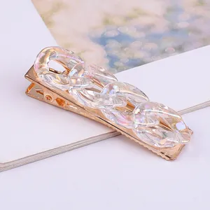 Macro view of an iridescent clear acrylic chain hair clip with a golden metal base