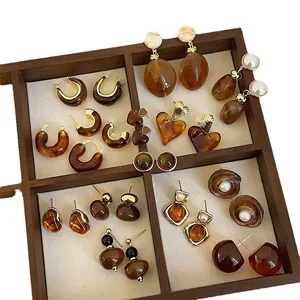Collection of vintage-style brown resin stud earrings and hoops in a wooden tray.
