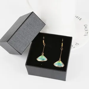 Elegante waaiervormige oorbellen met iriserend wolkenpatroon in een geschenkdoos.