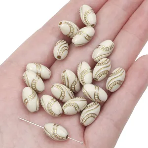 Macro view of beige oval acrylic beads with gold-traced vintage patterns for DIY jewelry making