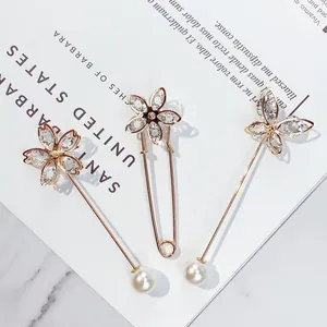 Detail eleganter Goldnadeln mit funkelnden Kristallen und weißen Perlen auf weißem Grund