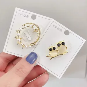 Nahaufnahme einer eleganten goldenen Perlenbrosche und süßen Eulen-Anstecknadeln