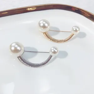Detail view of minimalist gold and silver U-shaped pearl brooches on a white ceramic plate