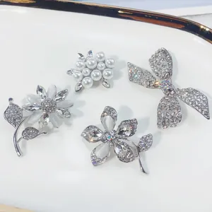 Detailansicht eleganter silberfarbener Blumen- und Schleifenbroschen mit Perlen und Steinen