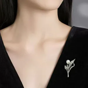 Nahaufnahme einer eleganten silbernen Blumenbrosche mit Perle auf schwarzem Kleid
