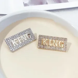 Nahaufnahme von gold- und silberfarbenen KING-Broschen mit Kristallen besetzt