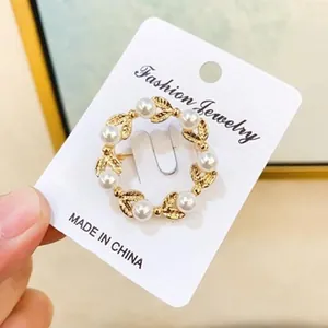 Detailansicht einer eleganten goldenen Kranz-Brosche mit Perlen auf weißer Karte.