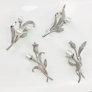 Detail von Vintage-Blumenbroschen aus Silberlegierung mit weißen Perlen auf weißem Grund.