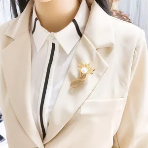 Detailansicht einer goldenen Vintage-Blumenbrosche mit Perle auf einem beigen Blazer.