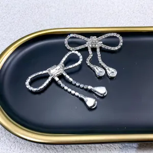Close-up of elegant silver bow brooch with tassels and full rhinestones on tray.