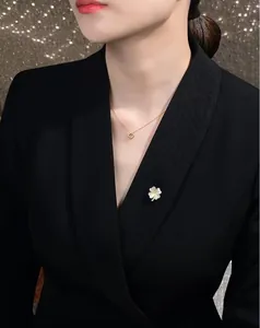 Nahaufnahme einer kleinen weißen Blumenbrosche als Verschluss an einem schwarzen Blazer.