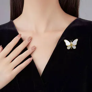 Elegante Schmetterlingsbrosche mit weißen Muschelflügeln und Perle auf einem Samtanzug.