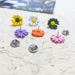 Close-up of colorful daisy enamel pins with butterfly clutch backings on paper.