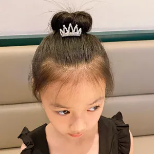 Young girl wearing a small silver rhinestone crown hair comb on a hair bun detail view